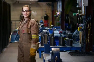 A female welder posing for pictures holding her helmet