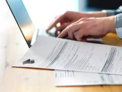 Young man writing college or university application form with laptop. Student applying to school. Scholarship document, admission paper or letter on table. Typing email. Education and communication.