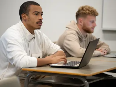 Two students in class taking notes on their laptops